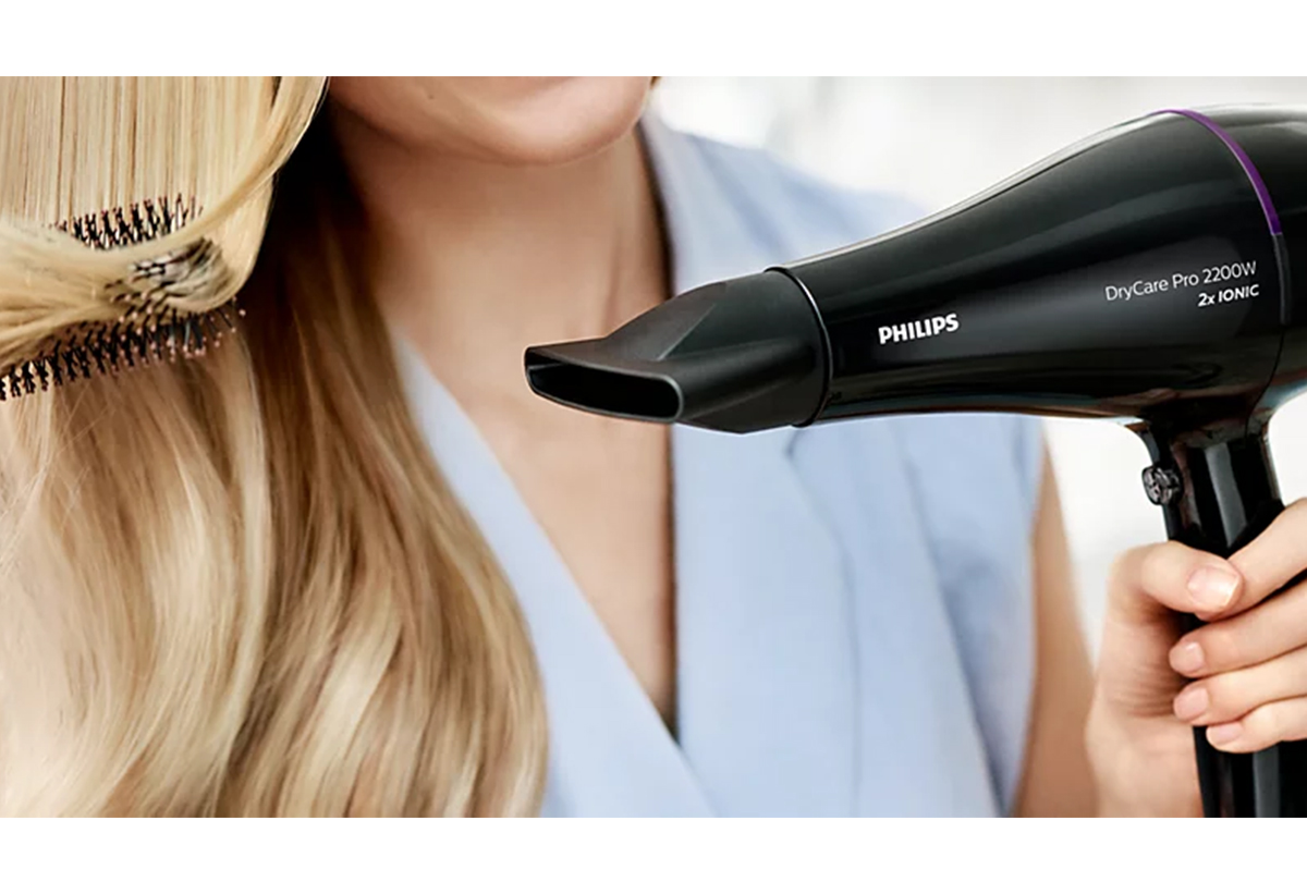 Μια γυναίκα στεγνώνει τα μαλλιά της με το στόμιο του σεσουάρ.